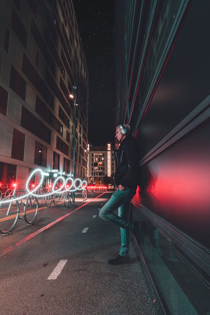 A man in Oslo leans against a wall with light trails creating dynamic patterns in the night cityscape.
